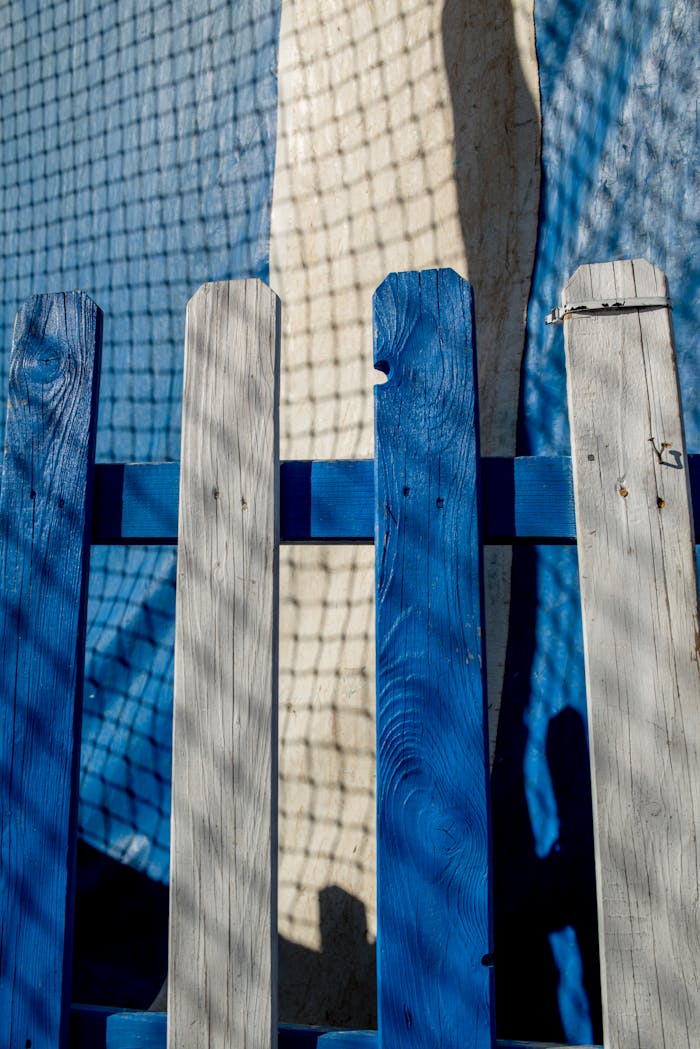 Artistic capture of a blue and white wooden fence casting shadows on a net background.